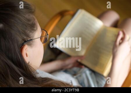 Ein Mädchen mit Brille liest bei Tageslicht ein Buch. Selektive Fokussierung auf Brillen. Stockfoto