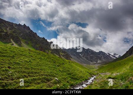 Idyllische Sommerlandschaft mit Wanderweg in den Bergen mit schönen frischen grünen Almen, blauem Himmel, Fluss und Brücke. Kirgisische Alatoo Mo Stockfoto