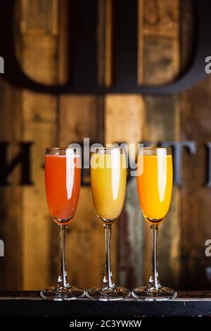 Drei verschiedene spritzige fruchtige Cocktails, rot, gelb und orange, in Flötengläsern Stockfoto