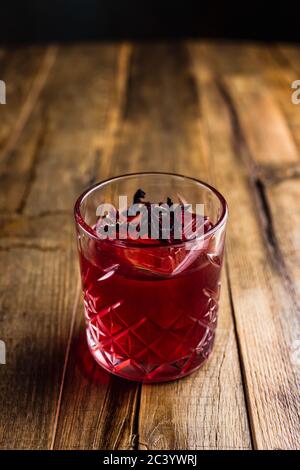 Ein Hibiskuscocktail mit einem Eiswürfel in einem Steinglas auf einem Holztisch Stockfoto