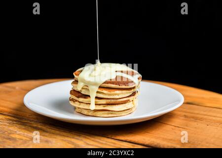 Ein Stapel Pfannkuchen mit Kondensmilch auf einem weißen Teller Stockfoto