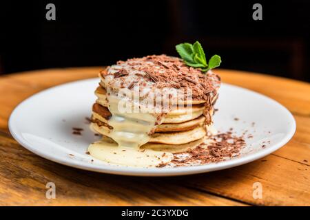 Ein Stapel Pfannkuchen mit Kondensmilch, Schokoladenbröseln und Minze auf einem weißen Teller Stockfoto