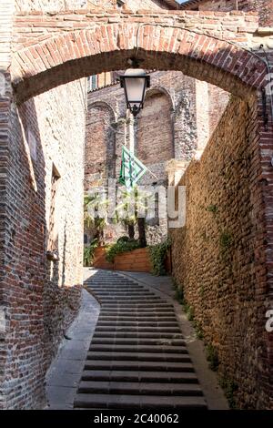 Ziegelbogen mit Treppe und schwarzer und grüner Flagge im Zentrum einer alten italienischen Stadt Stockfoto