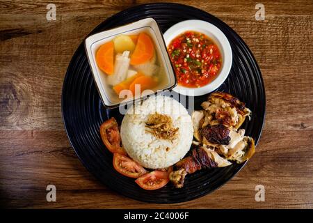Hühnerreis mit gehacktem, geröstetem Huhn, serviert mit scharfem Chili-Sambal und Hühnersuppe. Mit Tomatenscheiben und gebratener Zwiebel auftoben. Stockfoto