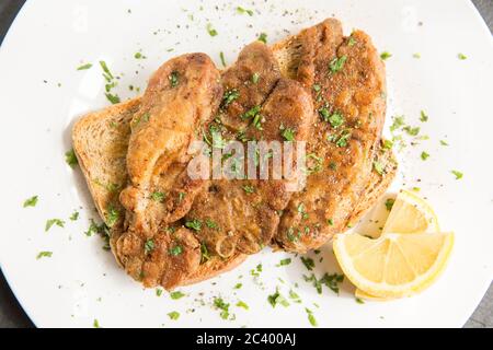 Die Lebern der Thornback-Strahlen, Raja clavata, die in Butter gebraten und auf Toast serviert haben. Garniert mit Zitronenscheiben und frischer Petersilie. Dorset Engha Stockfoto