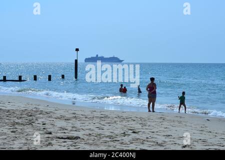 Boscombe, Bournemouth, Dorset, Großbritannien, 23. Juni 2020, Hitzewelle. Die Leute am Strand genießen am Morgen die heiße Sonne, während ein verankertes Kreuzfahrtschiff in der Nähe des Ufers sitzt. Stockfoto