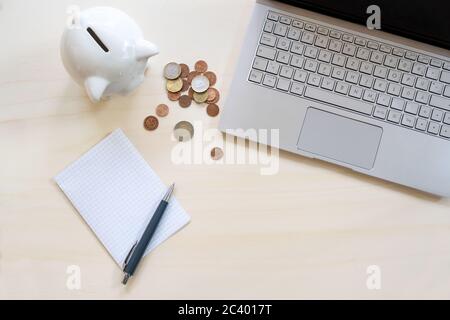 Budget-Konzept, Laptop, Sparschwein mit einigen Münzen und ein leeres Papier mit Stift auf einem Holzschreibtisch, Berechnung der Wirtschaft, um Geld zu sparen, Kopierer Platz, hoch ein Stockfoto