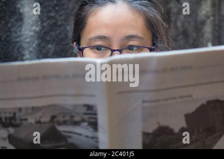 Eine Indonesierin mittleren Alters mit Brille und Zeitung Stockfoto