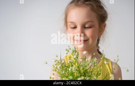 Nahaufnahme Porträt eines fröhlichen lächelnden kleinen Mädchen in gelb gekleidet hält Bündel von Feld Blumen in den Händen. Studio Shot isoliert auf weiß Stockfoto