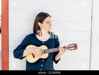 Junge stilvolle Brünette Mädchen spielt Ukulele. Stockfoto