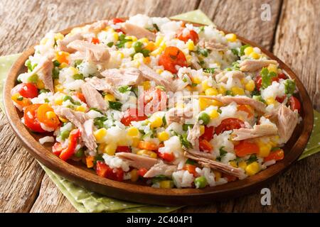 Salat aus Reis, Thunfisch, Tomaten, Paprika, Mais, grünen Erbsen und Kräutern in einer Platte auf dem Tisch. Horizontal Stockfoto