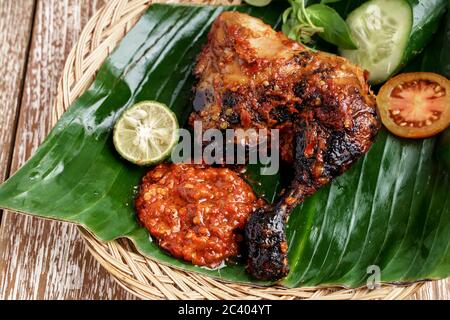 Nahaufnahme von gegrilltem Hähnchen mit Sambal Terasi und Scheiben von frischem Gemüse, frischen Tomaten, Gurken, Basilikum und Limette Stockfoto