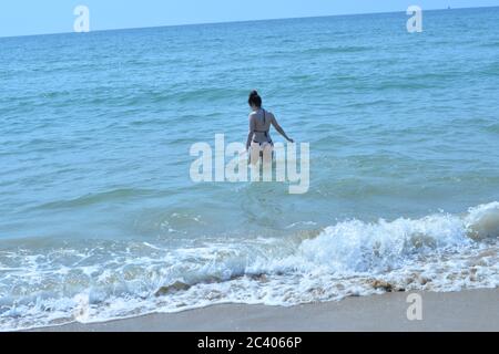 Eine junge Frau in einem knappen Bikini wagt sich in der heißen Sonne ins blaue Meer, Bournemouth, Dorset, Vereinigtes Königreich, 23. Juni 2020, Wetter. Es entsteht eine Hitzewelle, und es wird erwartet, dass die Temperaturen 30 Grad erreichen. Stockfoto