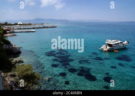 Griechenland, die Insel Agistri, in der Nähe von Athen. Kristallklares Wasser. Felsige Kiefernbedeckte Klippen. Ein sonniger Sommertag. Ausflugsboote, blaues Meer. Stockfoto