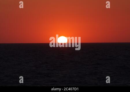 Sequenz von Bildern eines Sonnenuntergangs vom gleichen Aussichtspunkt Sonnenuntergang in den Meereshorizont, oranger Himmel bei Sonnenuntergang, Crimson Sonnenuntergang über dem Meer, Golden Orb trifft auf das h Stockfoto