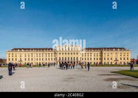 Blick auf Schloss Schönbrunn und Touristen, die im Hintergrund durch den klaren blauen Himmel laufen. Stockfoto