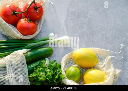 Null-Abfall-Shopping-Konzept. Frisches Gemüse und Obst in umweltfreundlichen Baumwollbeuteln auf Steintisch. Draufsicht, flach lagen Tomaten, Gurken, Zitronen, gr Stockfoto