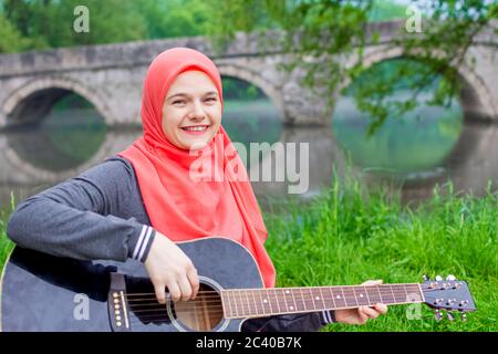 Happy Muslim Mädchen versuchen, akustische Gitarre auf dem Flussufer zu spielen Stockfoto