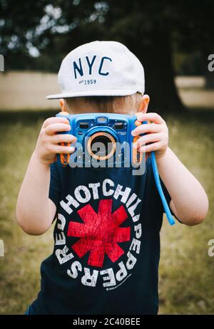 Ein kleines Kind im Freien und trägt eine Baseballmütze und T-Shirt ein Fotografieren mit einer Kamera für Kinder entwickelt Stockfoto