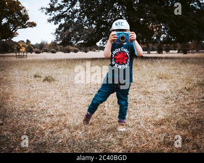 Ein kleines Kind im Freien und trägt eine Baseballmütze und T-Shirt ein Fotografieren mit einer Kamera für Kinder entwickelt Stockfoto