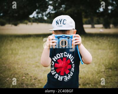 Ein kleines Kind im Freien und trägt eine Baseballmütze und T-Shirt ein Fotografieren mit einer Kamera für Kinder entwickelt Stockfoto