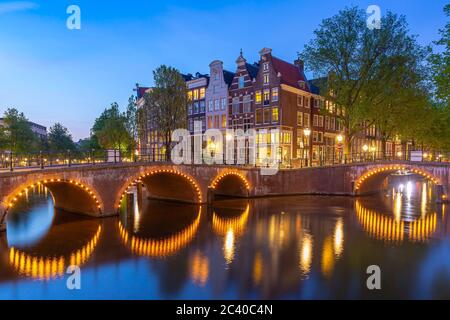 Amsterdamer Straßen und Kanäle in der Dämmerung. Brücken beleuchtet, Sommersaison. Beliebtes Reiseziel für Touristen. Stockfoto