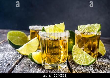 Goldene Tequila-Aufnahmen. Drei Tequila Schnapsgläser mit Salz- und Limettenscheiben, auf Holzhintergrund kopieren Raum Stockfoto