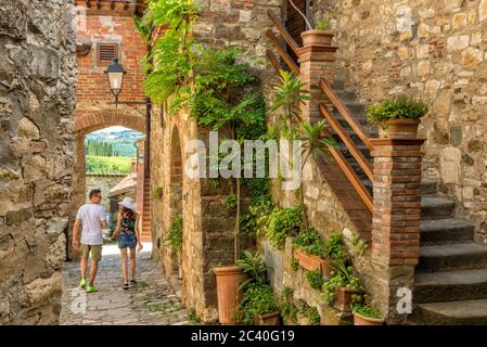 Ein paar Touristen gehen eine Gasse des Dorfes Montefioralle, in der Nähe von Greve in Chianti, im warmen Licht während eines Sommerurlaubs in der Toskana Stockfoto