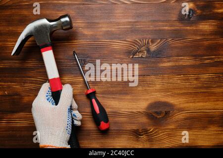 Hand in Arbeit Handschuhe hält Hammer und Schraubendreher auf Holzhintergrund mit Kopierraum Stockfoto