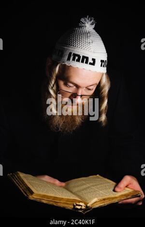 chassidischer jude beim Lesen der Tora. Religiöser orthodoxer jude mit Seitengelenken und rotem Bart in weißem Ballen, der im Dunkeln betet. Low-Key-Foto. Vertikale Ausrichtung Stockfoto