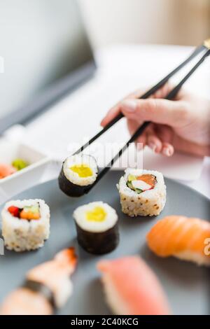 Geschäftsfrau beim Sushi neben ihrem Laptop. Nehmen Sie japanische Lebensmittel und Online-Bestellkonzept. Stockfoto
