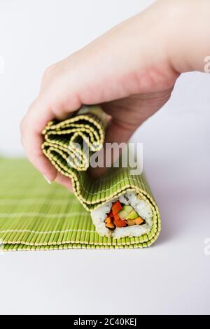 Nahaufnahme von Küchenchefs, die Sushi auf einer Bambusmatte auf weißem Hintergrund hochrollen. Japanische Gerichte. Stockfoto