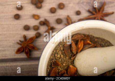 Piment in einem Keramikmörtel und verstreute Knoblauchzehen, Sternanis und Piment auf einem Holztisch. Nahaufnahme Stockfoto