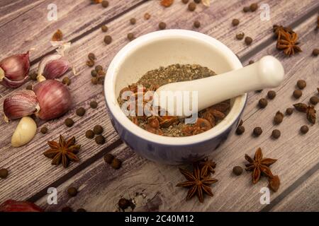 Piment in einem Keramikmörtel und verstreute Knoblauchzehen, Sternanis und Piment auf einem Holztisch. Nahaufnahme Stockfoto