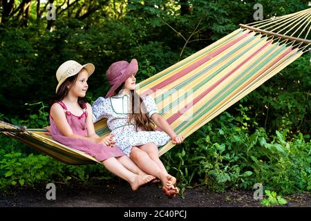 Zwei kleine Mädchen in einem Hut sitzen auf einem Helle Hängematte Stockfoto