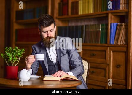 Literatur, Klassiker, Bibliothek, Nachmittagstee Konzept. Der Leser sitzt in luxuriösem Interieur und liest Buch. Bärtiger Mann im formellen Anzug mit einer Tasse englischen Tee. Reifer Mann mit nachdenklichen Gesicht genießt Lesen. Stockfoto