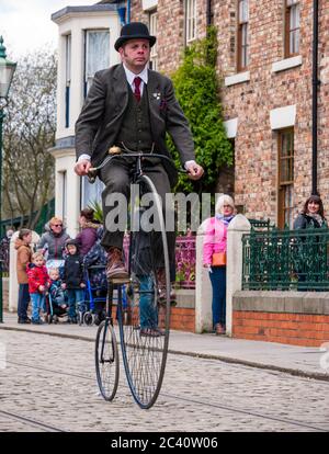 Mann, der Penny Farthing Vintage Fahrrad in Zeitkostüm reitet, Beamish Museum, Durham County, England, Großbritannien, Stockfoto