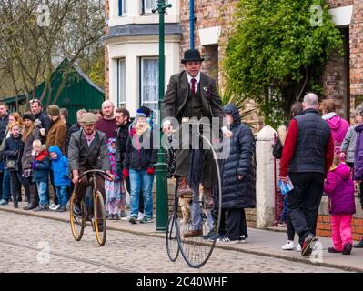 Mann in historischen Kostüm Reiten Vintage Penny Farthing altmodischen Fahrrad in 1900s Stadt, Beamish Museum, Durham County, England, Großbritannien Stockfoto