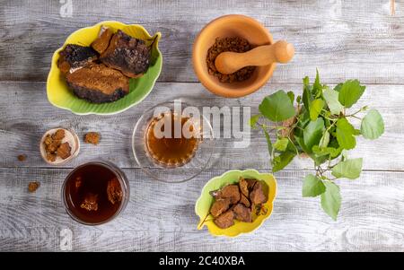 Heilende Infusion aus Birkenpilz Chaga, Zutaten für seine Küche und grünen Birkenzweigen auf Holztisch. Chaga Kaffee oder Tee. Getränke verbessern Stockfoto