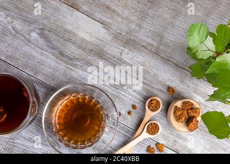 Heilendes Getränk von Birke Pilz chaga in Glas Tasse und chaga Stücke auf diagonalen Holztisch. Trendige Superfood. Chaga Pilz Kaffee oder Tee. Ändern Stockfoto