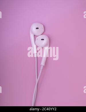 Schöne Ohrhörer. Weiße Ohrhörer auf pastellrosa Hintergrund. Musik ist mein Lebenskonzept. Valentine-Konzept. Weltmusik-Tag. Stockfoto