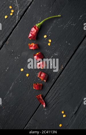 Getrockneter roter Chilischote auf schwarzem Holztisch in Stücke geschnitten Stockfoto