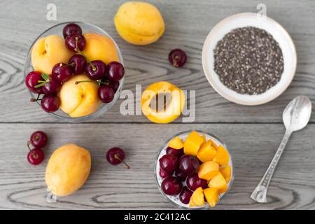 Gesundes veganes Frühstück mit Chia-Samen-Pudding mit frischen Aprikosen und Kirschen. Mehr Obst und Vintage Silber Löffel im Holzhintergrund. Stockfoto