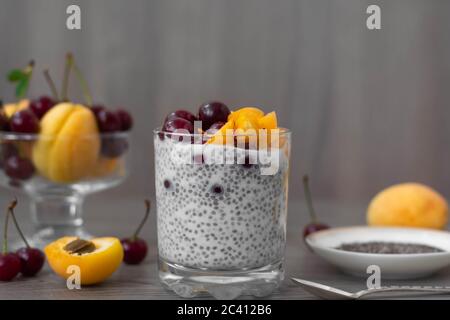 Gesundes veganes Frühstück mit Chia-Samen-Pudding mit frischen Aprikosen und Kirschen. Mehr Obst und Vintage Silber Löffel im Holzhintergrund. Stockfoto