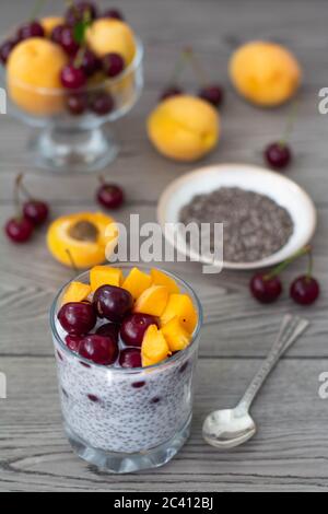 Gesundes veganes Frühstück mit Chia-Samen-Pudding mit frischen Aprikosen und Kirschen. Mehr Obst und Vintage Silber Löffel im Holzhintergrund. Stockfoto