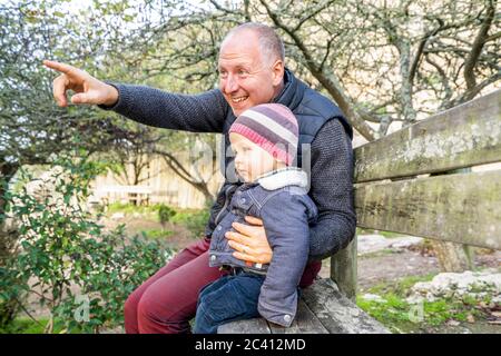 Vater und kleiner Sohn sitzen auf der Holzbank im Park Stockfoto