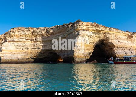 Landschaft mit den berühmten Benagil Höhlen, klarem blauen Himmel, Sandsteinklippen und Ausflugsboot an der Algarve Küste in Portugal Stockfoto