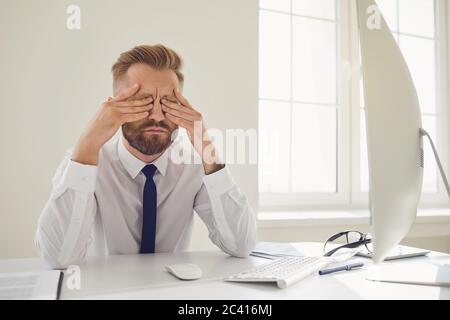 Ein ernstzunehmender Unternehmer liest Arbeitsdokumente, die mit einem Computer im Büro an einem Tisch sitzen. Stockfoto