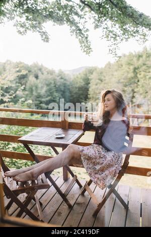 Junge redhaid Frau trinkt Kaffee auf Baumhaus Balkon Stockfoto