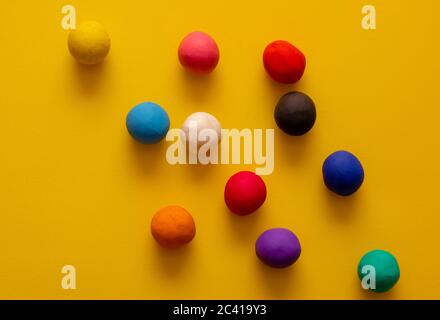 Viele verschiedene farbige Plastilin Kugeln auf gelbem Hintergrund. Bunte Top-Down-Ansicht, handgerollte Kinderspielzeug Stockfoto